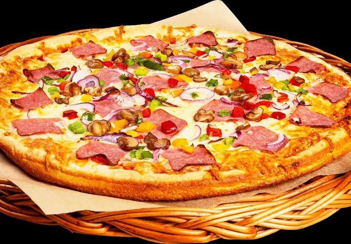 En stor pizza med skinke, grønnsaker og fargerike biter av frukt, servert i en kurv.