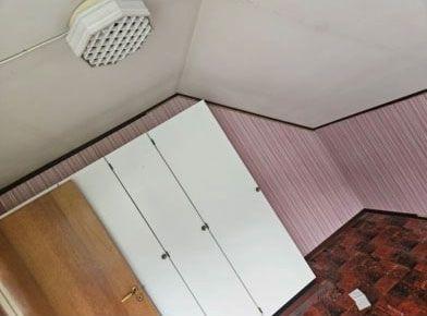 Rom med skråtak, hvite skap på veggen, rosa tapet og brunt gulv.
