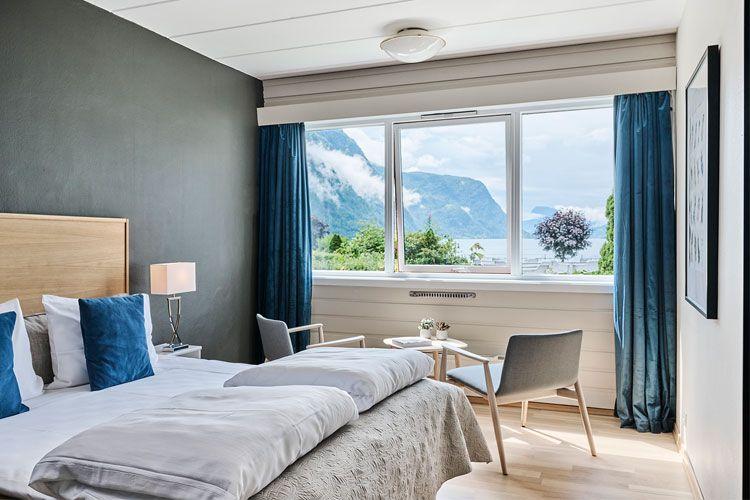 Moderne hotellrom med utsikt over fjell og innsjø, lyse farger og komfortable møbler.