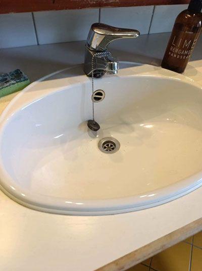 Vask med kran og avløp, plassert på en benkeplate i et bad.