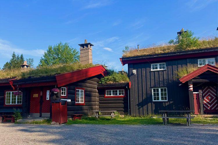 Tradisjonelt norsk hytte med torvtak, røde detaljer og grønne omgivelser under blå himmel.
