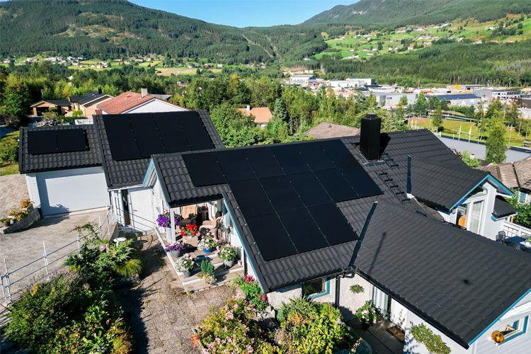 Moderne hus med solcellepaneler på taket, omgitt av grønn natur og fjell i bakgrunnen.