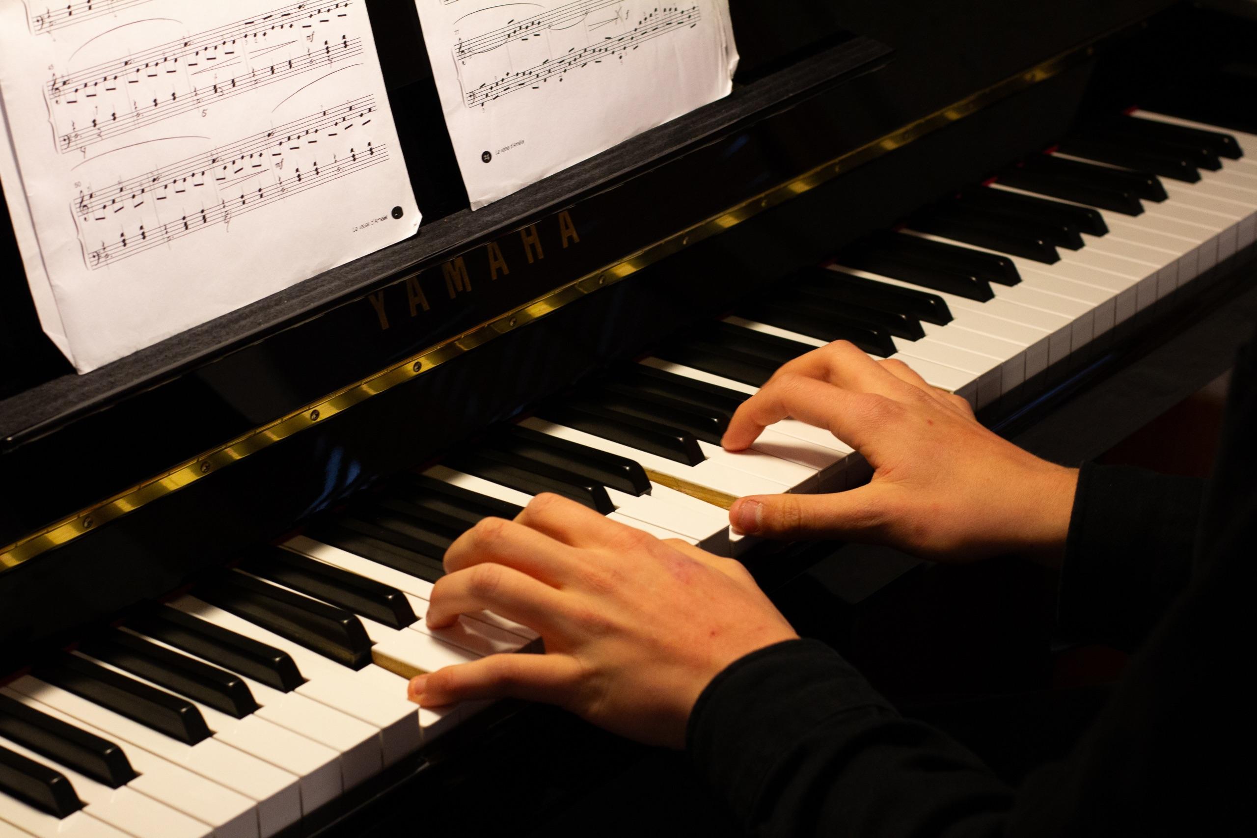 Hender som spiller piano med noter synlig i bakgrunnen.