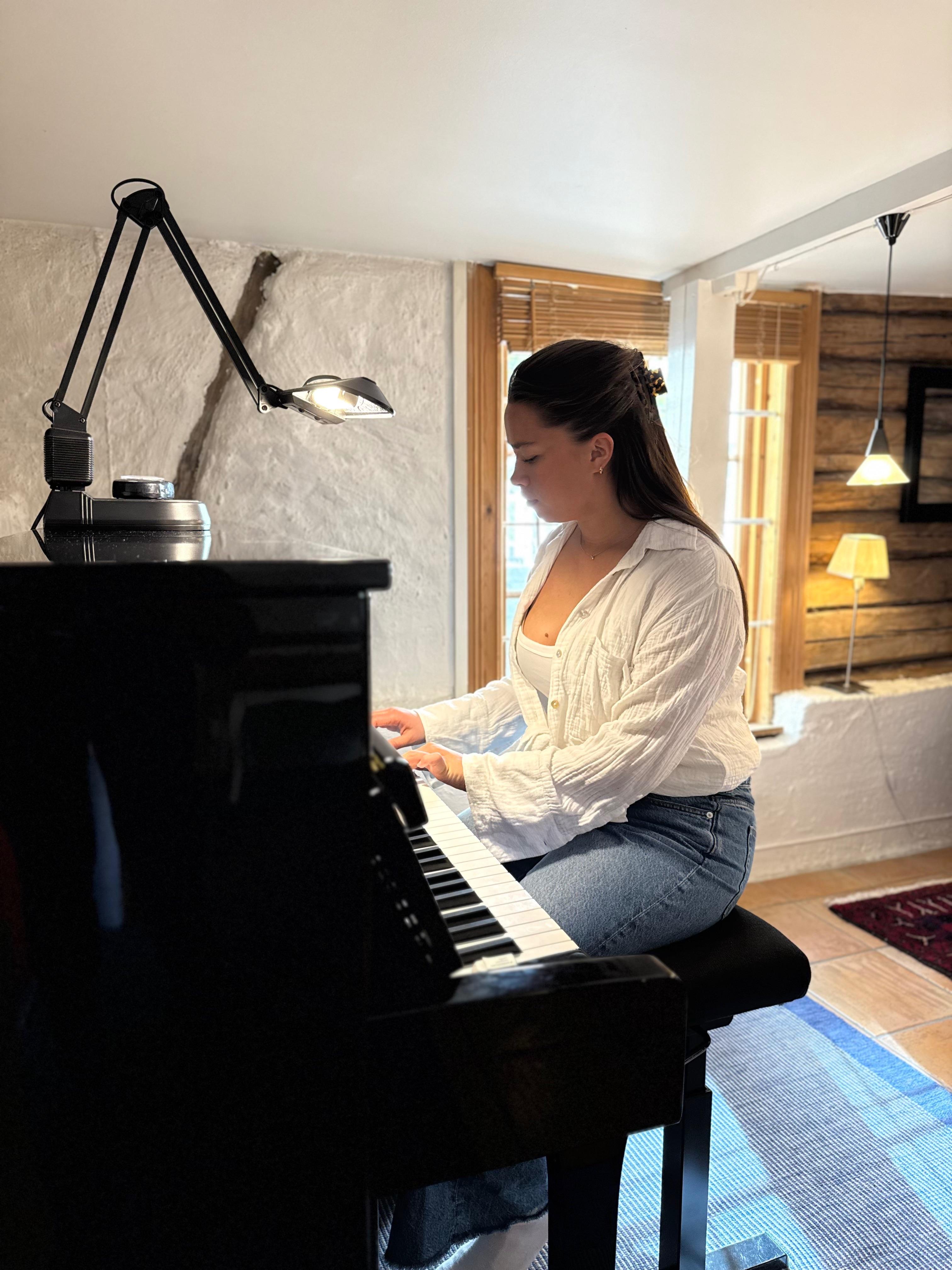 En kvinne spiller piano i et koselig rom med naturlig lys og moderne interiør.