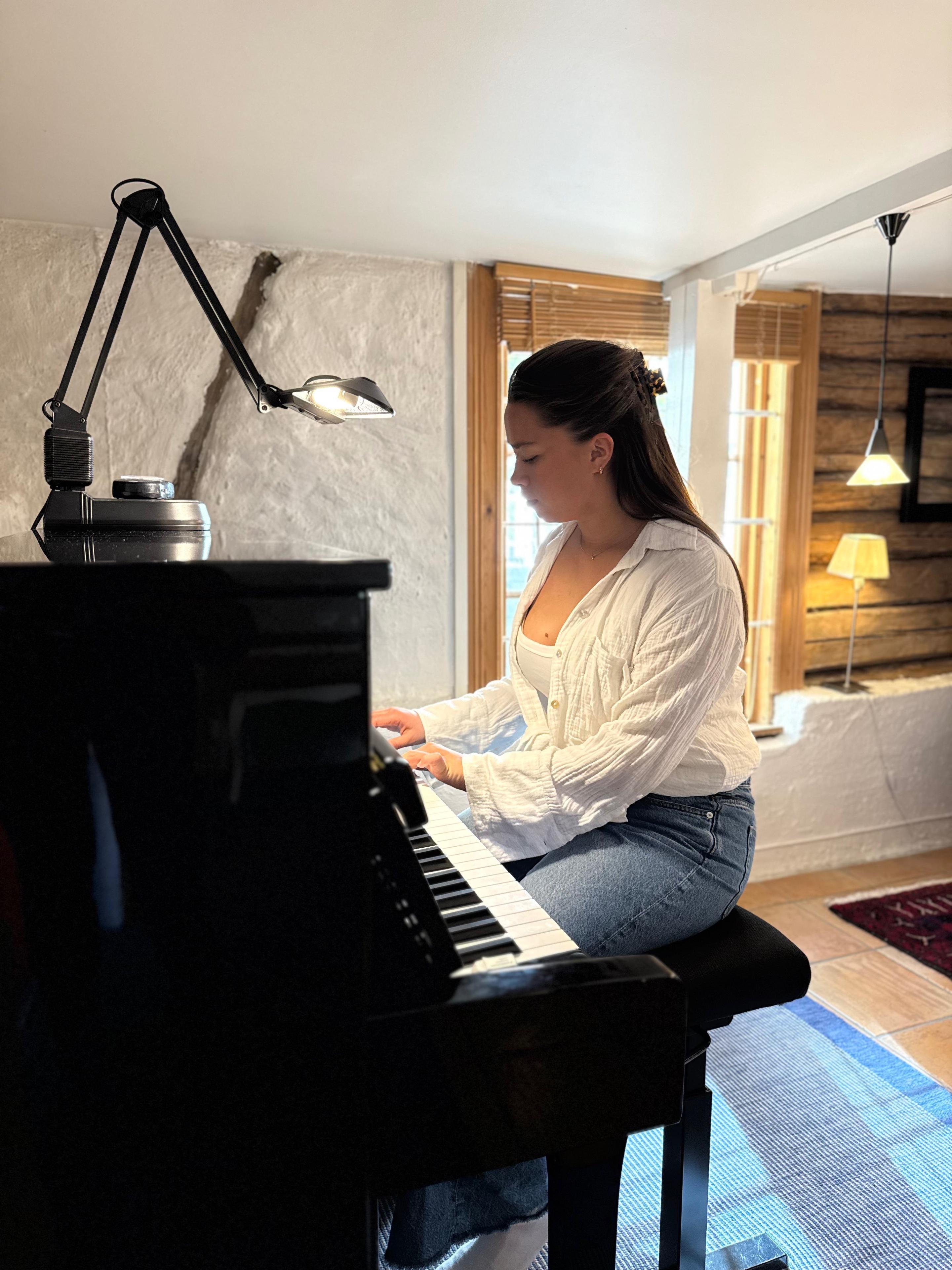 En kvinne spiller piano i et koselig rom med naturlig lys og moderne interiør.
