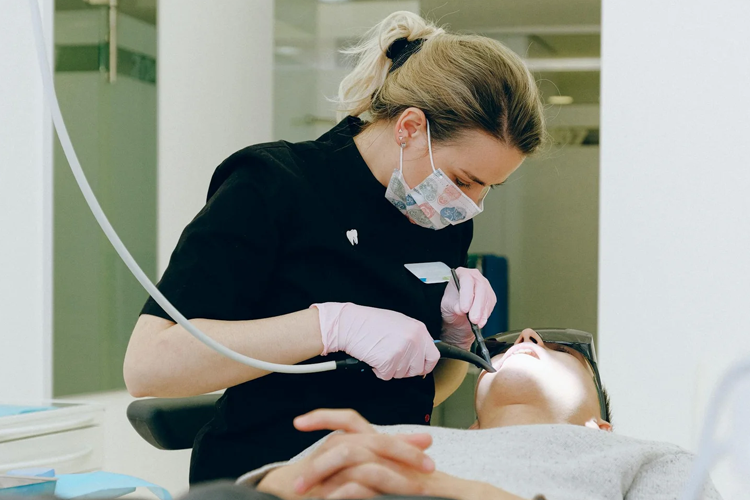 Tannlege som behandler pasient med dentalutstyr i moderne klinikk. Pasienten ligger i tannlegestolen.