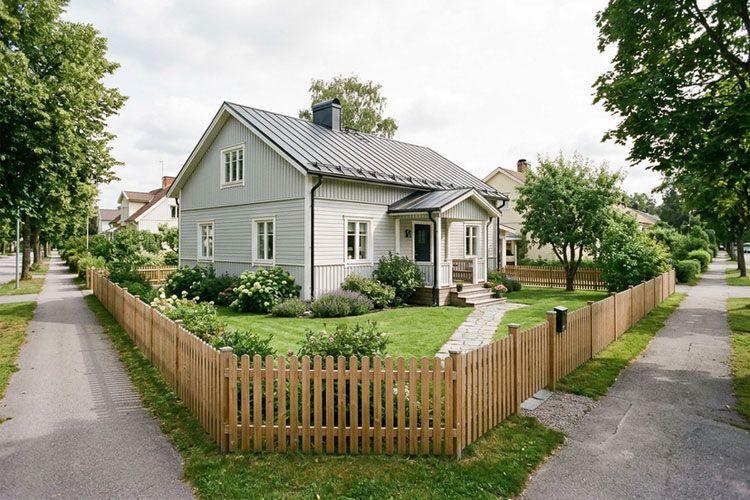 En koselig, hvit enebolig med skråtak, omkranset av en treplankegjerde og frodig hage.