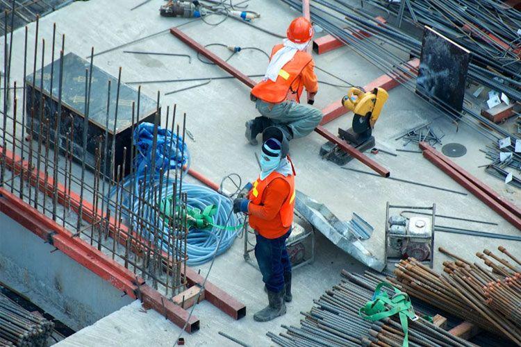Bygningsarbeidere i sikkerhetsutstyr jobber med stålstenger og verktøy på en byggeplass.