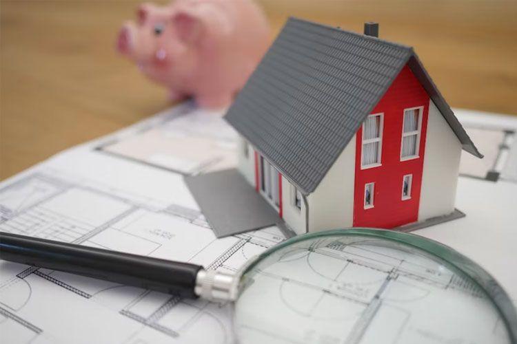 Modellhus på byggeplaner med forstørrelsesglass og sparegris i bakgrunnen.