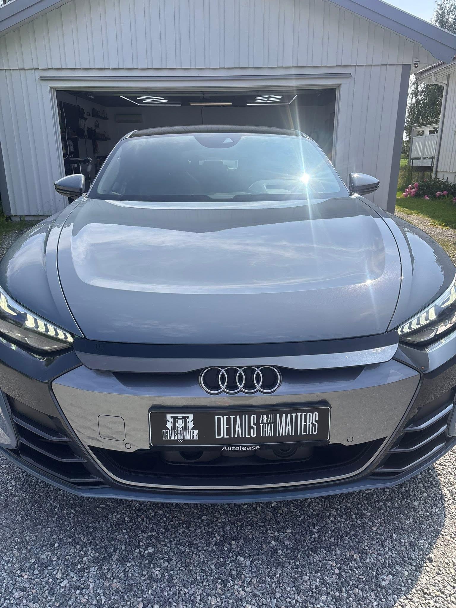 En grå Audi med moderne design står foran en garasje på en solfylt dag.