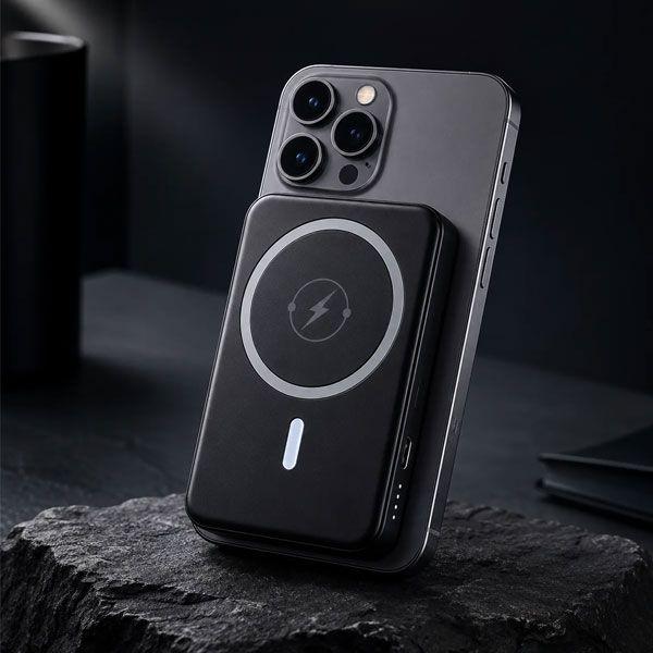 En svart trådløs powerbank som lader en iPhone 13, plassert på en mørk overflate.