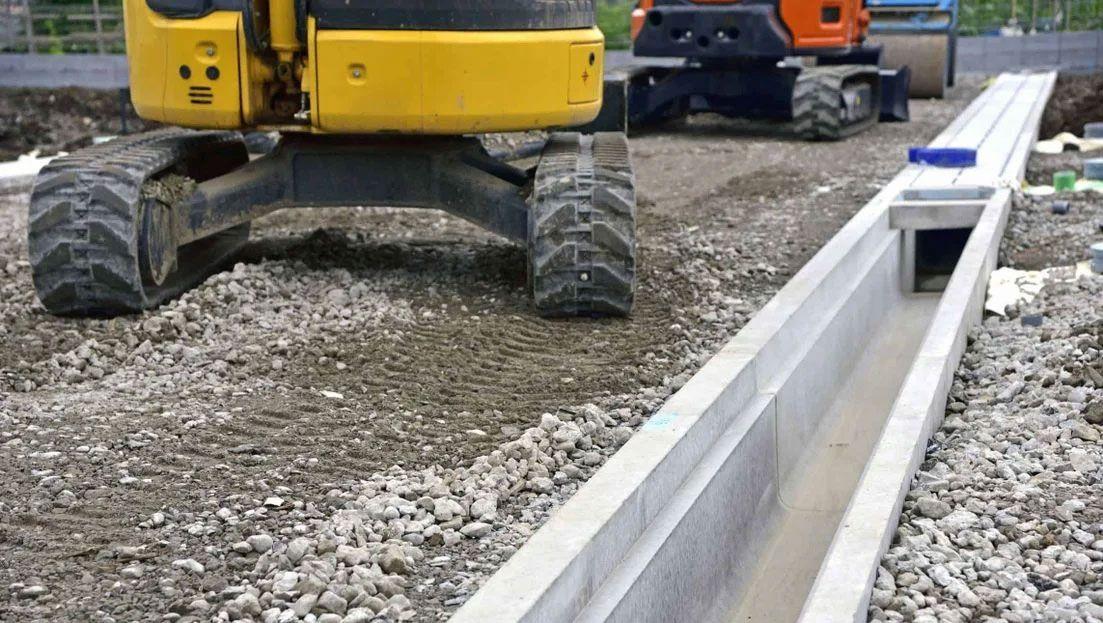 Grå grus med en gravemaskin og en betongrenne på byggeplassen.