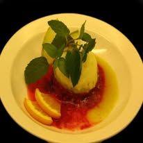 En dessert med sitron, mynteblader og bærsaus på en hvit tallerken.