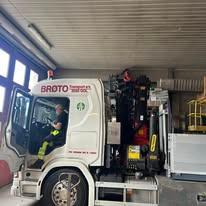 En lastebil med en sjåfør sitter inne i en garasje, med utstyr synlig på lastebilens bakside.