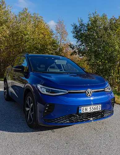 Blå Volkswagen ID.4 SUV parkert på en grusvei med trær i bakgrunnen.