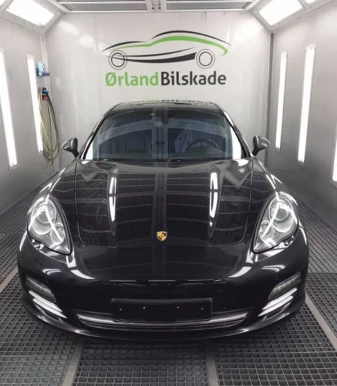 En svart Porsche Panamera i en bilverksted med lys og verktøy i bakgrunnen.