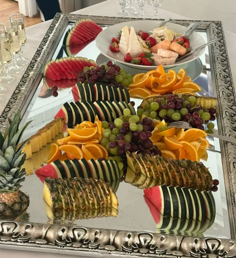 Et dekorativt fruktfat med vannmelon, ananas, druer, appelsiner og jordbær på et speil.