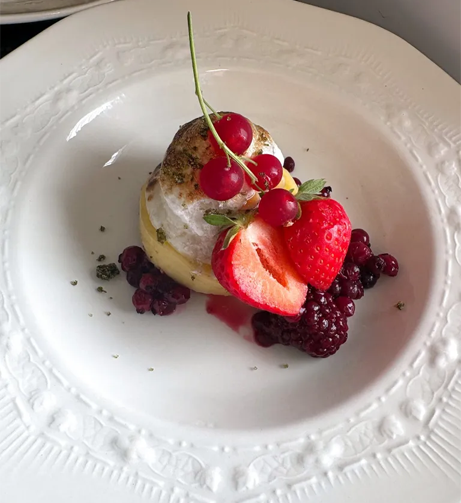 En delikat dessert med marengs, friske bær som jordbær og rips, servert på en hvit tallerken.