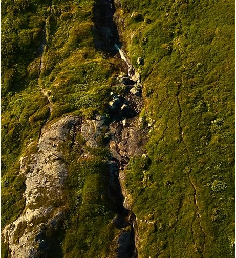 En fjellside dekket av grønt gress og steiner, med en tydelig kløft som går nedover.