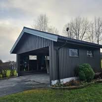 Moderne, grått hus med skråtak og garasje, omgitt av grønt gress og trær.