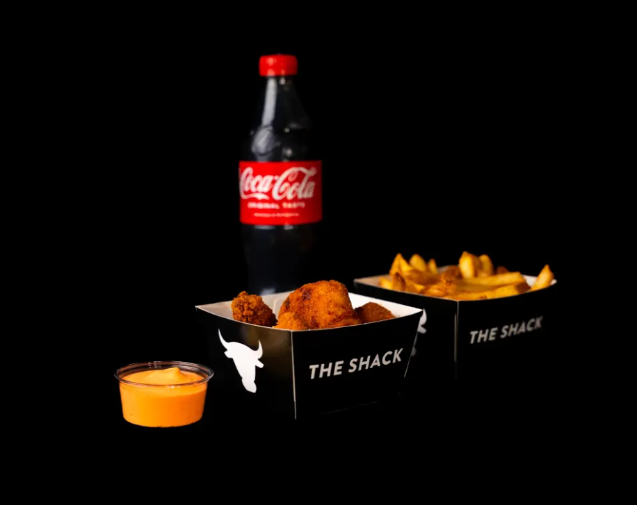Kyllingbiter med pommes frites og en flaske Coca-Cola fra The Shack, servert på svart bakgrunn.