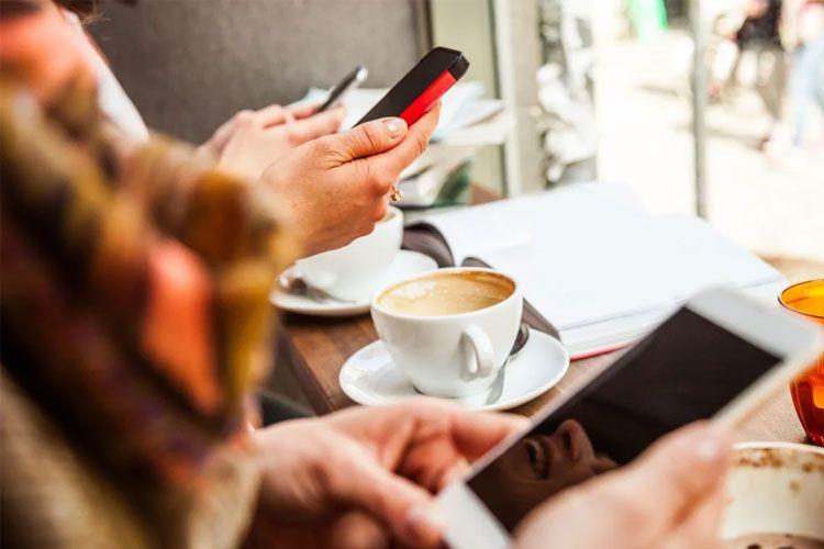 Hender som holder smarttelefoner ved et kafébord med kaffekopper og notater i bakgrunnen.