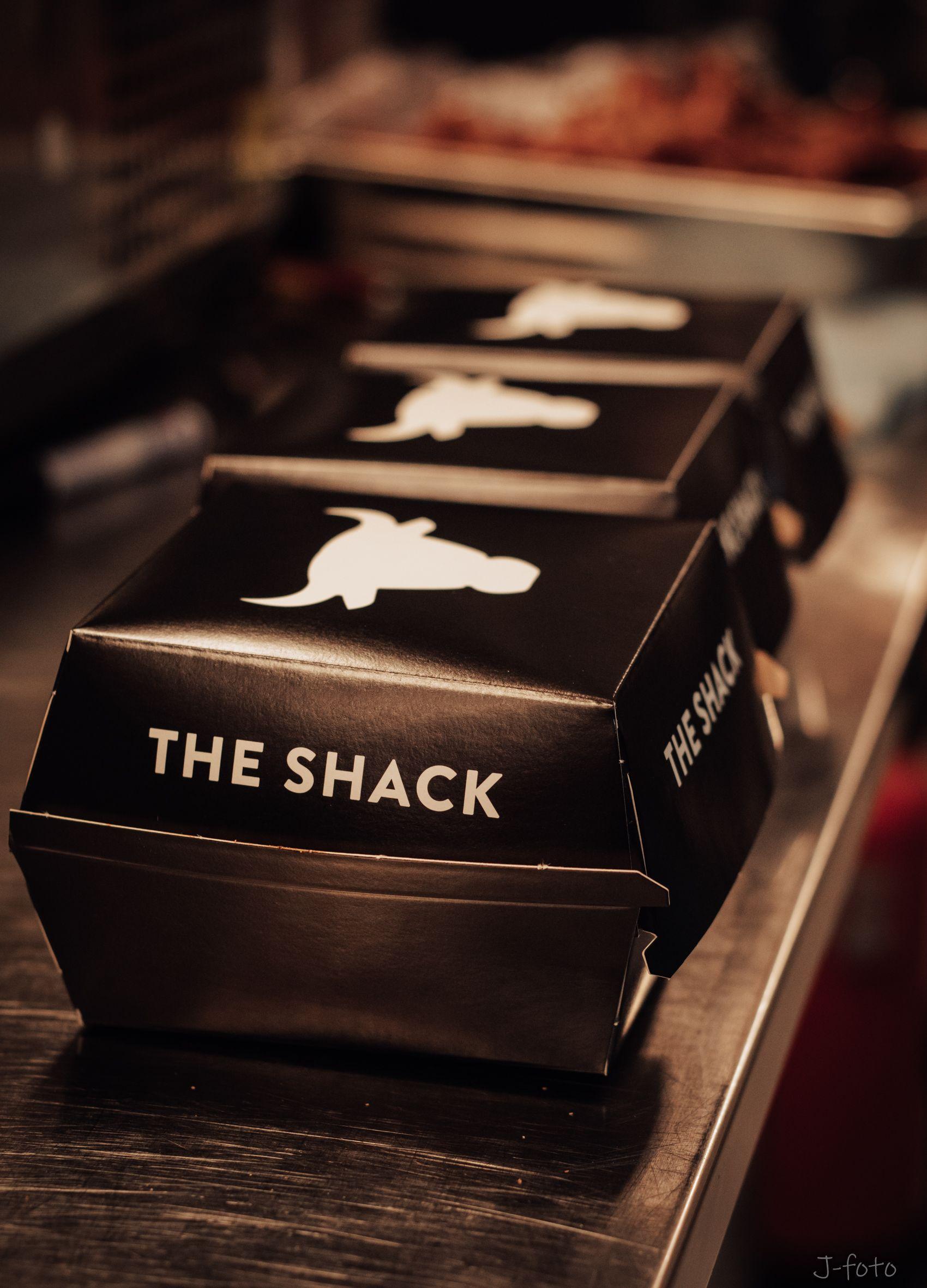 Svart take-away esker med teksten "THE SHACK" på en benk i en restaurant.