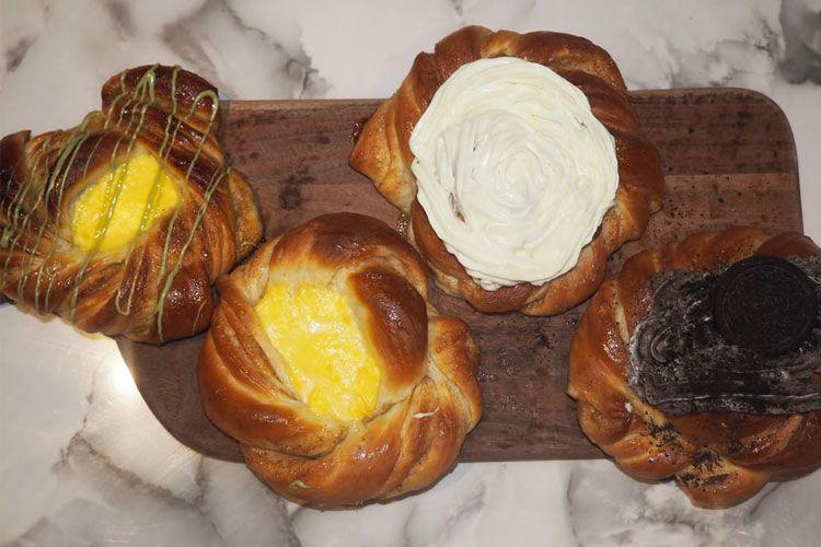 Fire forskjellige bakverk på en treplate, inkludert kanelbolle, sitronfylling og sjokoladeglasur.