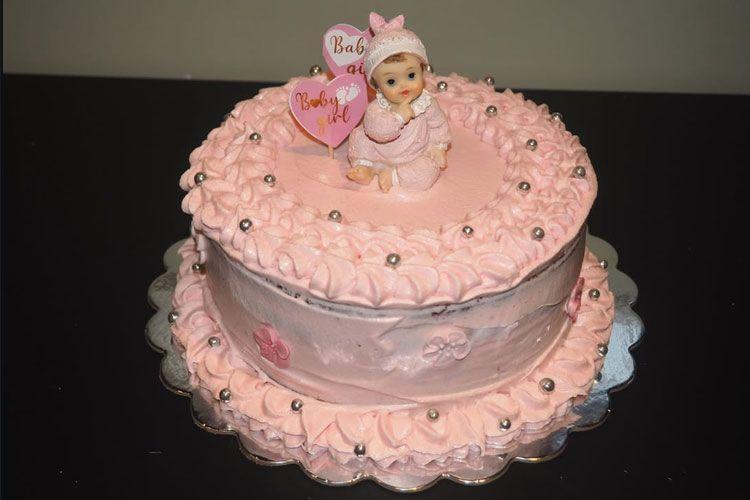 En rosa bursdagskake med en dukke og hjerteformede dekorasjoner på toppen.