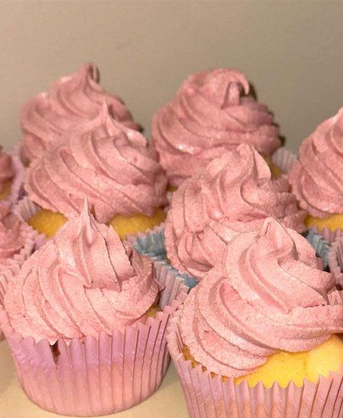 Flere cupcakes med rosa frosting i papirformer, plassert på en lys bakgrunn.