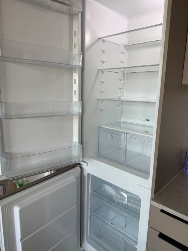 Åpen hvit kjøleskap med tomme hyller og fryser nederst, plassert i et moderne kjøkken.