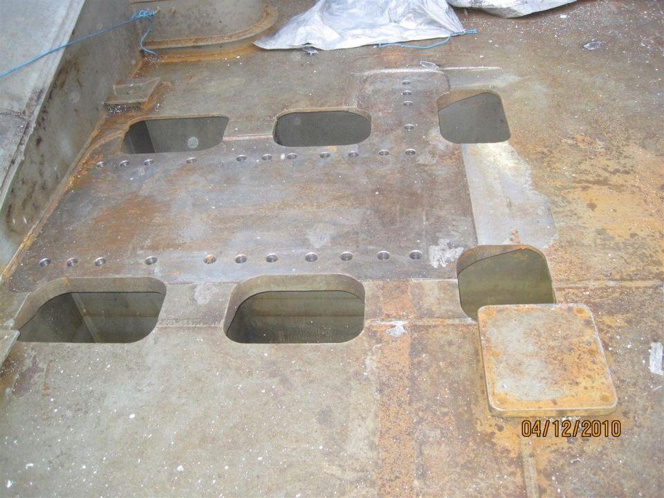 Åpent område med flere hull i metallplaten, synlig rust og sveisesømmer på overflaten.
