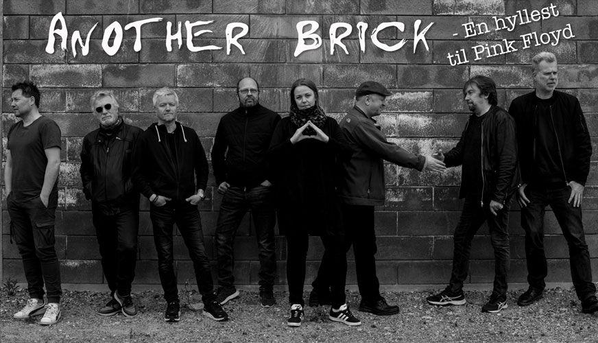 Bandet Another Brick står foran en murvegg, med tekst som hyller Pink Floyd. De har ulike klær og uttrykk.