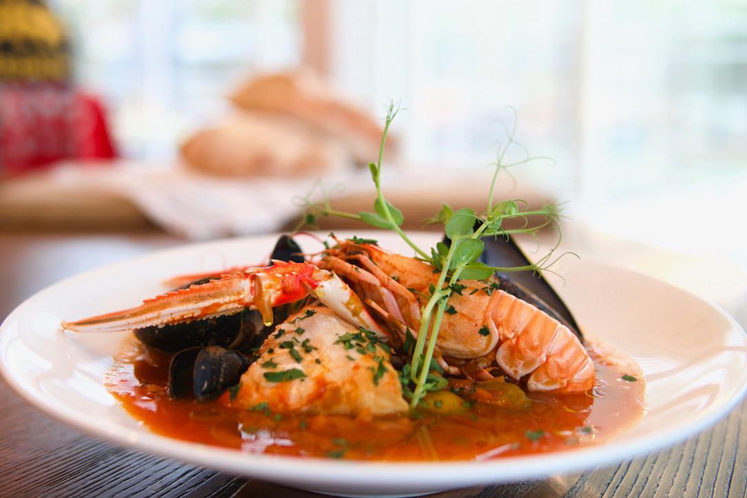En tallerken med sjømat, inkludert reker, krabbe og fisk i en tomatsaus, pyntet med friske urter.