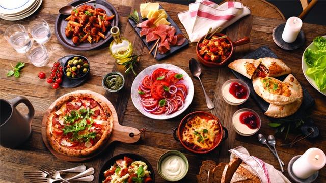 Et variert bord med italiensk mat, inkludert pizza, pasta, skinke, oliven og salater.