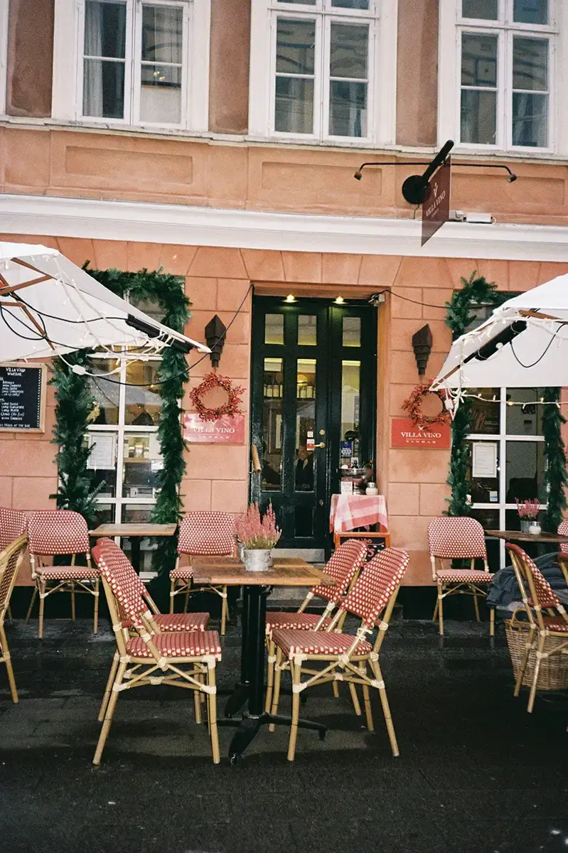 En terrasse med flere stoler og parasoller, med utsikt over gaten og bygninger i bakgrunnen, som skaper en koselig utendørs spiseatmosfære.