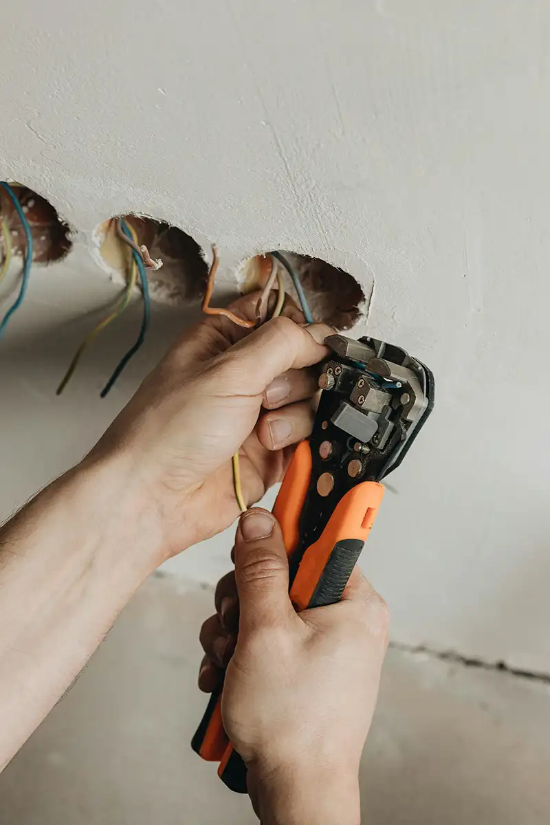 En person bruker en ledningsavisolator for å fjerne isolasjonen fra elektriske ledninger som stikker ut fra hull i en vegg.